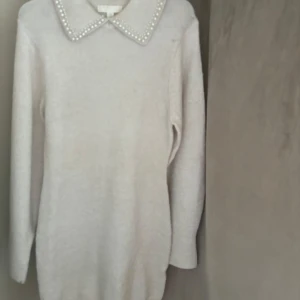 Vit stickad klänning med pärldetaljer - Säljer en superfin vit stickad tröja från H&M i storlek XS. Den har långa ärmar och en snygg krage dekorerad med pärlor som ger en elegant touch. Perfekt för både vardag och festliga tillfällen. Tröjan är i mycket bra skick och redo för en ny ägare!