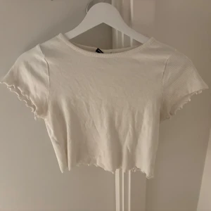 Vit croppad topp - Säljer en söt vit croppad topp med korta ärmar och ribbad struktur. Toppen har en enkel och stilren design som passar till det mesta. Den är i bra skick.