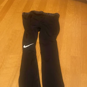 Svarta träningsbyxor från Nike - Säljer ett par svarta träningsbyxor från Nike i bra skick. De har en tight passform och är perfekta för träning. Byxorna har en elastisk midja och det klassiska Nike-loggan i vitt på benet. Perfekta för gymmet eller löprundan!