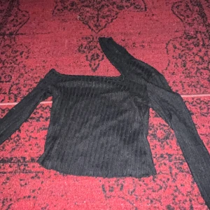Svart ribbad oneshoulder topp - Snygg svart ribbad topp med oneshoulder-design. Perfekt för en utekväll eller fest. Den har en tight passform som framhäver figuren och ger en stilren look. Materialet är mjukt och stretchigt för extra komfort.