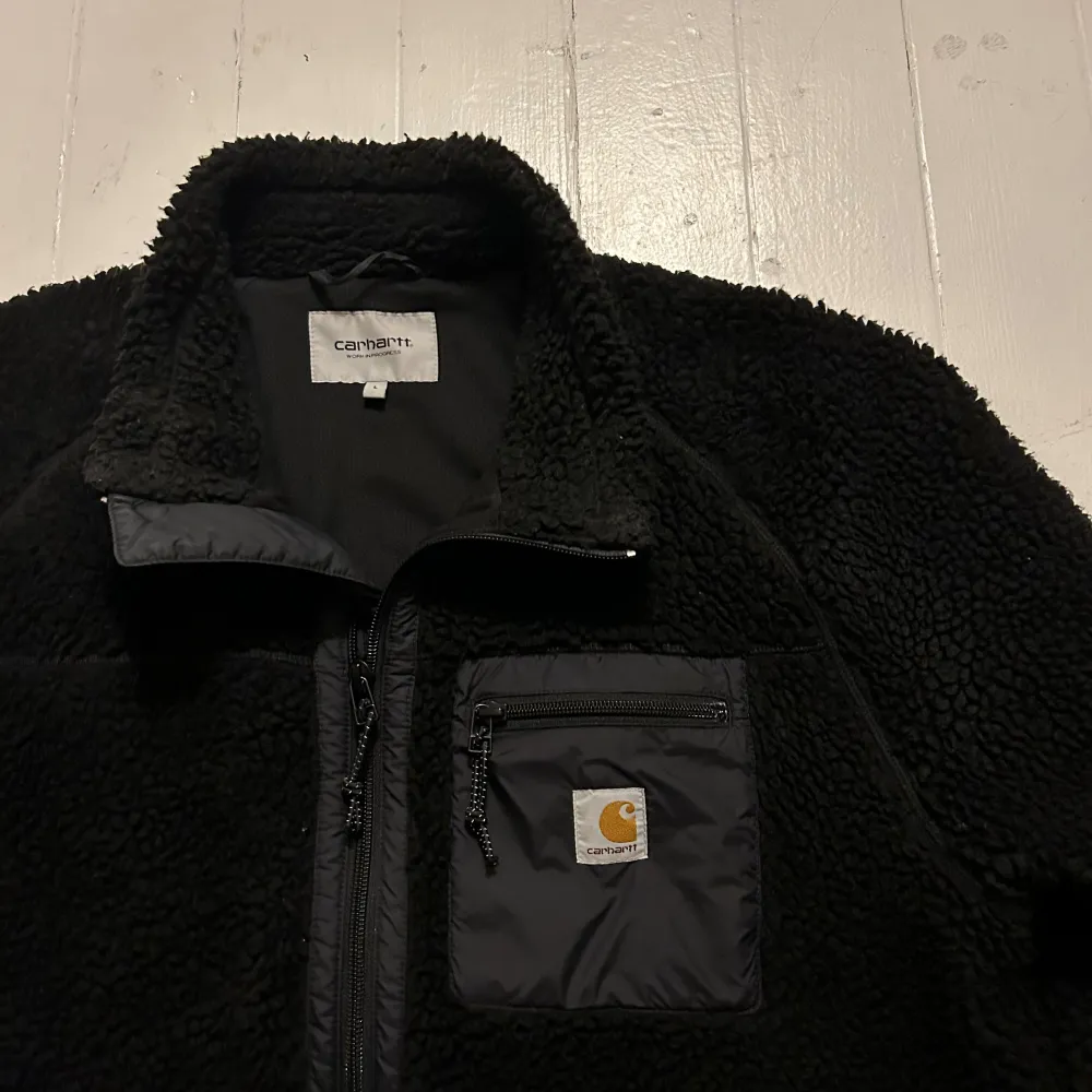 Säljer en svart fleecejacka från Carhartt i storlek L. Jackan har en dragkedja framtill och en praktisk bröstficka med dragkedja. Perfekt för kyliga dagar och har en mysig, varm känsla. Passar både till vardags och utomhusaktiviteter. Priset jag sätter kan diskuteras! Meddela vid frågor. . Jackor.