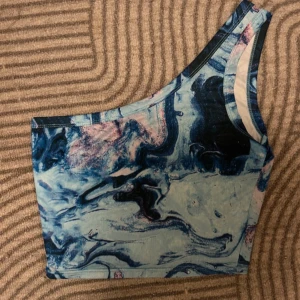 Marmorerad oneshoulder topp - Säljer en supercool blå oneshoulder topp med ett unikt mönster som ser ut marmor Toppen är tight och framhäver figuren på ett snyggt sätt