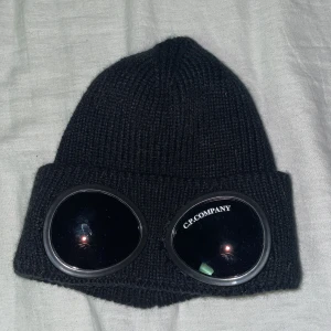 Svart mössa från C.P. Company - Säljer en svart stickad mössa från C.P. Company då den är för liten för mig och inte används! Mössan är i mycket bra skick och gjord av 100% bomull. Mössan är i liten storlek dock!!! Säljer för endast 350kr!
