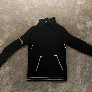 Säljer en snygg svart hoodie från Balmain med coola dragkedjedetaljer på fickorna och ärmarna. Den har en quiltad design på axlarna och en hög krage med snörning. Perfekt för höst och vinter, både stilren och bekväm. Passar lika bra till vardags som till fest!