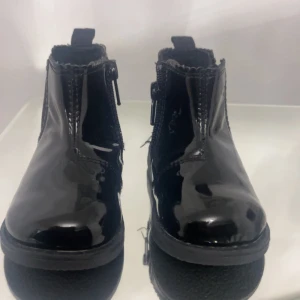 Svarta lackade boots med dragkedja - Snygga svarta boots i lackat material med dragkedja på sidan för enkel på- och avtagning. Perfekta för både vardag och fest med sin blanka yta som ger en stilren look. Sulan är robust och ger bra grepp. Passar perfekt till höst- och vinteroutfits!