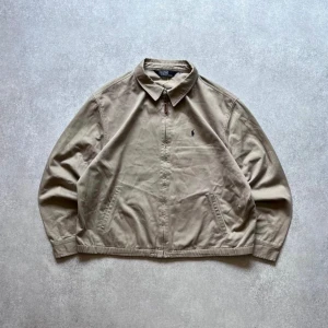 Polo Ralph Lauren jacka beige - Säljer en snygg beige jacka från Polo. Den har en klassisk krage och dragkedja framtill med ett läderdetalj. Jackan är långärmad och har en broderad logga på bröstet. Perfekt för vår och höst!