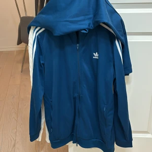 Adidas tracksuit - Fin blå Adidas tracksuit, köpt på Adidas i Spanien. Tracksuit; dvs både koftan/tröjan och byxorna ingår. Fint skick på dem, alltid tvättade enligt anvisningar. Färg: Blå Storlek: L på tröjan & XL på byxorna Byxorna passar dock även L då de spänns åt