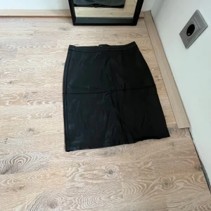 Svart skinnkjol med dragkedja - Snygg svart skinnkjol i en klassisk stil. Kjolen har en dragkedja framtill och är perfekt för både vardag och fest. Den är i ett tidlöst snitt som passar till många olika outfits. Perfekt för höst och vinter! Skriv för fler bilder eller frågor❤️