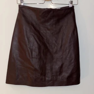 Brun skinnkjol från H&M - Säljer en snygg brun skinnkjol från H&M i äkta läder. Kjolen har en stilren design med en dragkedja baktill som ger en cool touch. Perfekt för höst och vinter, och kan enkelt stylas för både vardag och fest. Passar perfekt för dig som vill ha en tidlös och chic look! Ordinarie pris 999 kr 