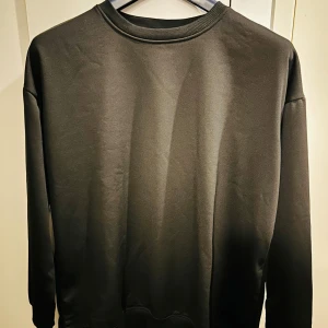 Svart tröja i polyester - Säljer en stilren svart tröja i 100% polyester. Perfekt för både vardag och chill. Tröjan har en enkel design med långa ärmar och rund hals. Skön och lätt att matcha med det mesta i garderoben. Passar bra till höst och vinter.