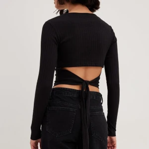 Svart ribbad topp från NA-KD - Säljer en superfin svart ribbad topp från NA-KD i storlek S. Den är croppad med långa ärmar och har en snygg öppen rygg med knytning. Perfekt för både vardag och fest! 🖤Bra skick, inga defekter.