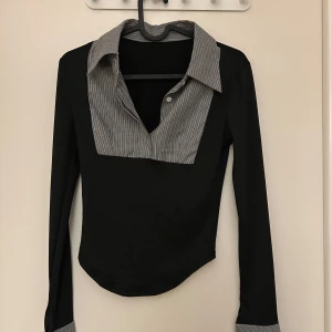 Svart långärmad topp med randig krage - Säljer en stilren svart långärmad topp med en snygg randig krage och manschetter. Perfekt för både vardag och fest! Materialet känns mjukt och bekvämt. Passar bra till jeans eller kjol för en chic look. Hör av dig vid intresse! 🖤