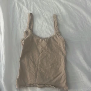 Beige linne från H&M Divided - Säljer ett enkelt och stilrent beige linne från H&M Divided. Perfekt för sommardagar eller som ett basplagg i garderoben. Linnet är ärmlöst och har en tight passform som sitter snyggt på kroppen.