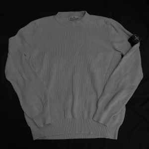 Grå ribbad tröja från Stone Island - Säljer en snygg vit ribbad tröja från Stone Island. Perfekt för höst och vinter, och den ikoniska loggan på ärmen ger en extra touch av stil. Passar både till vardags och lite finare tillfällen. Om du har några frågor är det bara att skriva. Kan bytas också 