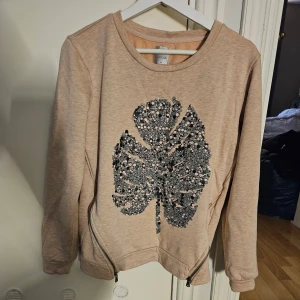 Tröja nytt  - Oanvänd Snygg tröja med tryck av ett blad i svart, grått och aprikosnypris 499 kr. Tröjan har blixtlås på sidorna och en liten stjärna på baksidan.