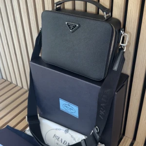 Prada Saffiano Leather Bag  - Prada Saffiano Leather Bag En otroligt fin axelremsväska som bör ses i verkligheten för bästa upplevelse.  -Storlek: Unisex (Axelrem som går att spänna ut samt in) -Skick: 9,5/10 -Nypris: 30000kr -Vårat pris: 15000kr -Frakt: (Hemleverat spårbart)📦