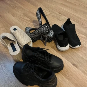 Olika skor till salu - Säljer ett gäng olika skor! Först har vi ett par svarta sneakers med tjock sula, perfekta för vardagsbruk. Sen finns det ett par glittriga pumps med spetsig tå och hög klack, idealiska för festliga tillfällen. Vi har också ett par svarta slip-on sneakers med vita sulor och glittriga detaljer, superbekväma och stiliga. Slutligen ett par beige sandaler med platåsula i ett stickat material, perfekta för sommaren.