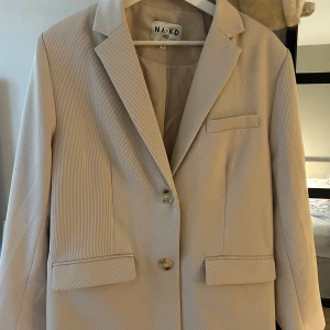 Beige kavaj - Beige kavaj från NA-KD i strl 38. Väldigt gott skick. Använd 2-3 gånger