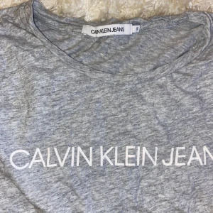Grå t-shirt från Calvin Klein Jeans - Säljer en snygg grå t-shirt från Calvin Klein Jeans i storlek. Passar toppen till både vardag och skola!!😜