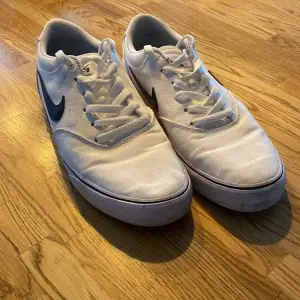 Säljer ett par vita Nike sneakers med den klassiska svarta Swoosh-loggan på sidan. Skorna har snörning och en bekväm passform. De är i välanvänt skick men fortfarande snygga och funktionella. Perfekta för vardagsbruk!