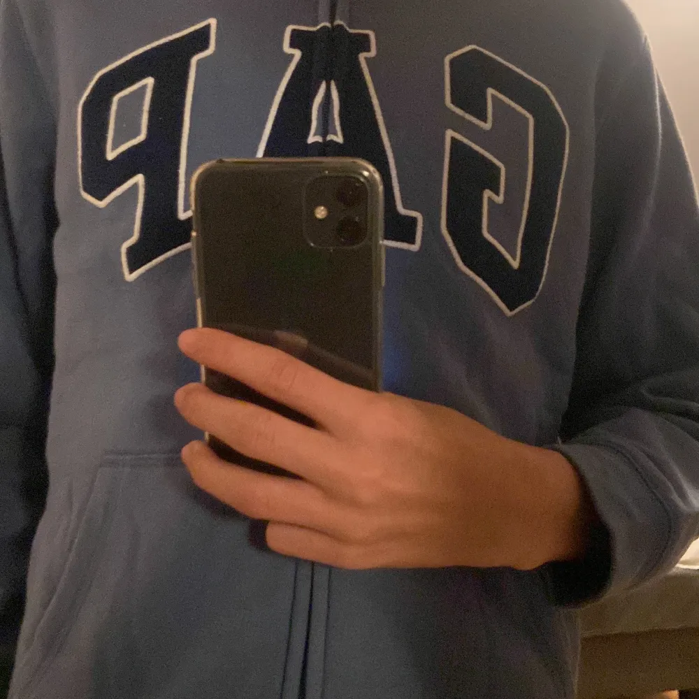Säljer en supermysig blå hoodie från GAP. Den har en stor logga på framsidan och en dragkedja hela vägen ner. Insidan är fodrad med mjuk fleece, perfekt för kyliga dagar. Den har långa ärmar och en praktisk huva. Perfekt för både vardag och chill!. Neuletakit & Villapaidat.