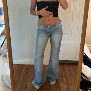 Ljusblå bootcut jeans - Säljer ett par snygga ljusblå bootcut jeans i bra skick. De är lågmidjade och har en klassisk femficksdesign med knappar och dragkedja. Perfekta för både vardag och fest! Passar till allt från sneakers till klackar.