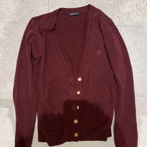 Vinröd kofta från Gina Tricot - Säljer en snygg vinröd kofta från Gina Tricot. Den har långa ärmar och knappar framtill. Perfekt för höst och vinter, och den är i bra skick. 