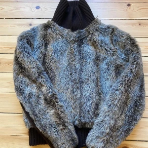 Grå pälsjacka med ribbad krage - Säljer en supermjuk och fluffig grå pälsjacka med en snygg ribbad krage och muddar. Perfekt för att hålla sig varm och stilren under kyliga dagar. Jackan har en cool och unik look som verkligen sticker ut. Passar perfekt för både vardag och fest!