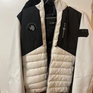 Vit och svart jacka från Sail Racing - Säljer en snygg vit och svart jacka från Sail Racing i medium. Jackan har en cool design med dragkedja och är perfekt för höst och vinter. Den är i bra skick men har en liten fläck på ärmen. Perfekt för dig som gillar stil och funktion!