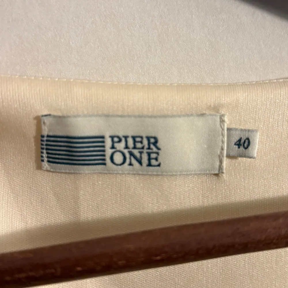 Säljer en elegant klänning från Pier One i storlek 40. Den har en stilren design med en ljus cremefärgad överdel och marinblå nederdel. Klänningen har en v-ringad urringning. Den har en dragkedja på sidan och är oanvänd.. Mekot.