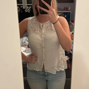 Vit ärmlös blus med spetsdetaljer - Säljer en söt vit blus med spetsdetaljer upptill. Den är ärmlös och har knappar framtill, perfekt för sommardagar eller en avslappnad vårlook. Blusen är i bra skick och passar till både jeans och kjol. Köparen står för frakten💖