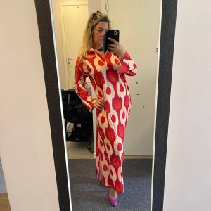 Röd och vit mönstrad långklänning - Säljer en superfin långklänning med ett coolt rött och vitt mönster. Klänningen har långa ärmar och en bekväm passform, perfekt för både vardag och fest. Den är helt ny och har en härlig retrostil. 