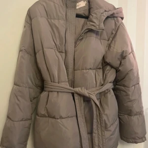 Beige pufferjacka från Nelly - Säljer en snygg beige pufferjacka från Nelly i storlek 38. Jackan har ett bälte i midjan och dragkedja framtill. Perfekt för kyliga dagar och ger en stilren look. Passar både till vardags och lite finare tillfällen.
