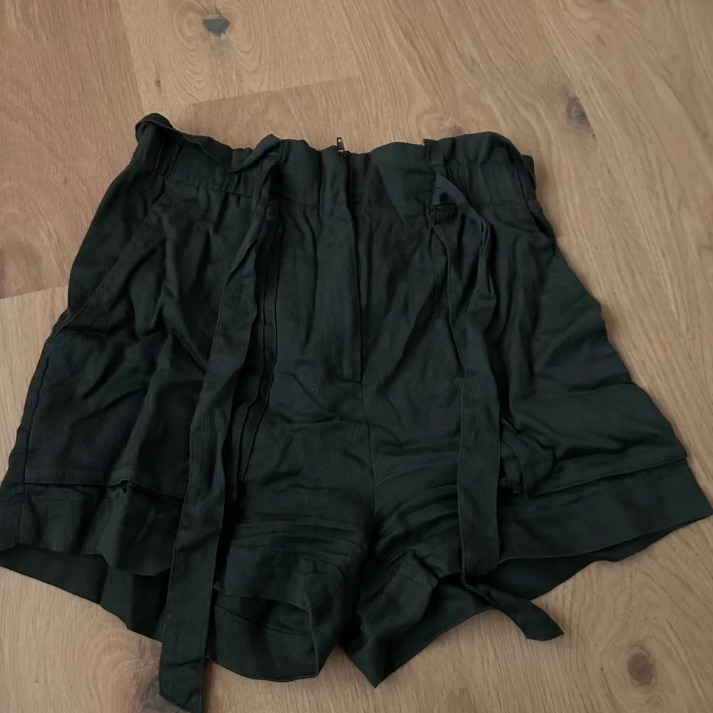 Säljer ett par militärgröna shorts i mycket bra skick. De har en högmidjad passform och är gjorda av ett mjukt material som känns skönt mot huden. Shortsen har knytband i midjan för justerbar passform och en stilren look. Perfekta för både vardag och fest!. Shorts.