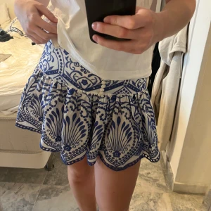 Vit och blå kjol från Zara - Superfin kortkjol från Zara i vitt och blått med ett snyggt mönster. Kjolen har knappar framtill och en volangdetalj. Storlek S. Använd fåtal gånger men är i fint skick utan defekter. 💕💕