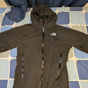 Svart jacka från The North Face - Säljer en svart jacka från The North Face i bra skick. Den har en praktisk huva och dragkedja framtill. Perfekt för höst- och vinterväder. Jackan är långärmad och har en stilren design med logotypen på bröstet och ryggen.