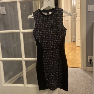 Svart och vit mönstrad klänning från H&M Divided - Snygg svart och vit mönstrad klänning från H&M Divided i storlek XS passar även S. Klänningen är ärmlös och har ett geometriskt mönster som ger en cool look. Perfekt för både vardag och fest!
