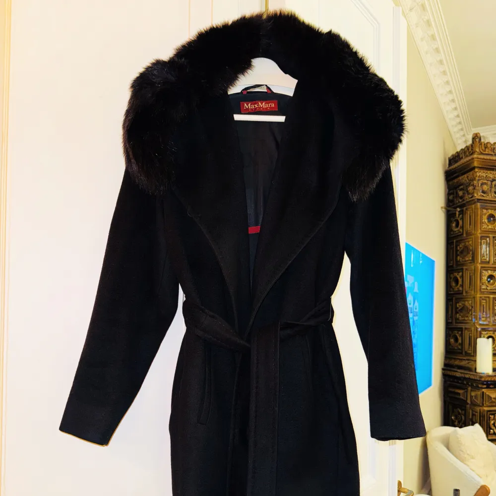 Säljer en elegant svart kappa från Max Mara i mycket bra skick. Den har en lyxig pälsdetalj runt kragen och ett knytbälte i midjan för en snygg passform. Perfekt för höst och vinter, med långa ärmar och en klassisk stil. Passar både till vardags och festliga tillfällen. Storlek 34.. Takit.