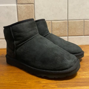Svarta UGG boots i mocka - Säljer ett par svarta UGG boots i mjuk mocka. De är perfekta för kalla dagar med sin varma insida. Skorna har en klassisk design med rund tå och är i bra skick. Perfekta för höst och vinter!