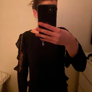 Svart långärmad topp med spetsdetaljer - Säljer en elegant svart långärmad topp med vackra spetsdetaljer längs ärmarna. Perfekt för en kväll ute eller en fest. Toppen har en normal passform och är i mycket bra skick. Passar perfekt till både jeans och kjol!