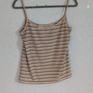 Randig linne från Amalia, Strl L - Säljer ett randigt linne från Amalia i storlek L. Linnet är i beige och svart med smala axelband. Tillverkat i 92% polyester och 8% lycra, vilket gör det stretchigt och bekvämt.