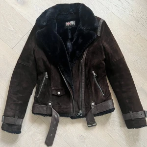 Brun mockajacka från Jofama design Kristine Ullebø - Brun mockajacka från Jofama by Kristine Ullebø. Jackan har en mjuk pälsfodrad krage och dragkedja framtill, bälte i midjan och flera fickor med dragkedjor. Perfekt för höst och vinter, jättevarm och mysig! Knappt använd och i perfekt skick! 