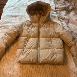 Beige pufferjacka från Zara - Säljer en superfin beige pufferjacka från Zara i storlek S. Den har en mysig huva och praktiska dragkedjor på fickorna. Perfekt för kyliga höst- och vinterdagar. 🍂❄️