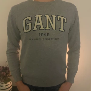 Grå tröja från GANT - Säljer en snygg grå tröja från GANT med tryck 'GANT 1949 New Haven, Connecticut' på framsidan. Tröjan är i bra skick och har långa ärmar med ribbade muddar. Perfekt för nästan allt. Tveka inte på att höra av er vid frågor och funderingar 🌟