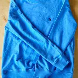 Blå tröja från Polo Ralph Lauren - Säljer en snygg ljusblå tröja från Polo Ralph Lauren.  Bara använd fåtal gånger. Den har en klassisk design med det ikoniska broderade logotypen på bröstet. Tröjan är i mycket bra skick och perfekt för både vardag och lite finare tillfällen. Passar bra till både jeans och chinos! Tveka inte vid frågor eller intresse! 