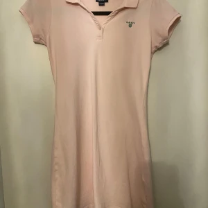 Ljusrosa klänning från Gant - Säljer en ljusrosa klänning från Gant i mycket bra skick. Den har en klassisk krage och korta ärmar, perfekt för vår och sommar. Materialet känns mjukt och bekvämt, idealiskt för både vardag och festligare tillfällen.