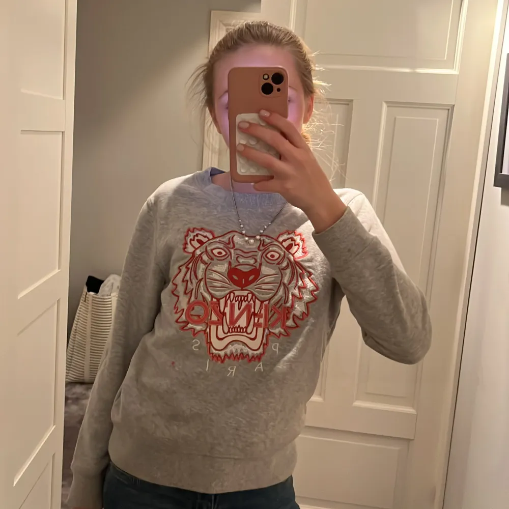 Säljer en grå sweatshirt från Kenzo med ett coolt tigertryck i rött och vitt. Tröjan är i bra skick men en liten röd fläck under märket och har långa ärmar. Perfekt för en avslappnad stil eller att bära till skolan. Superbekväm och stilren! Passar en 11-13 åring (själv på bilden är jag 13). Tröjor & Koftor.