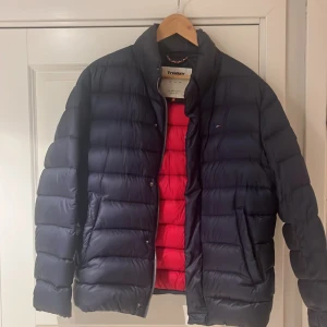 Mörkblå dunjacka från Tommy Hilfiger - Säljer en snygg mörkblå dunjacka från Tommy Hilfiger jeans i storlek M. Jackan har en cool röd insida och är perfekt för kalla dagar. Den är långärmad och har en dragkedja framtill. Passar perfekt för både höst och vinter. Har haft jackan i 3 år men inga defekter finns. Så har tagit väl hand om den😊