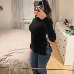 Svart polotröja från Boohoo - Säljer en stilren svart polotröja i mycket bra skick. Den är stretchig och perfekt för både höst och vinter. Tröjan har långa ärmar och är supermjuk och bekväm, med en slits på varsin sida av midjan. Passar perfekt till jeans eller kjol för en snygg vardagslook. 