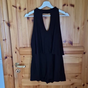 Svart ärmlös klänning - Säljer en stilren svart jumpsuit med en djup v-ringning och öppen rygg. Jumpsuiten är ärmlös och är perfekt för festliga tillfällen. 